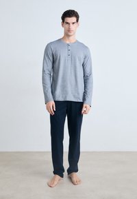 Camisa henley de manga larga gris con placket de tres botones, combinada con pantalones elásticos de cintura oscura en color marino, ambos hechos de una tela suave y lisa.