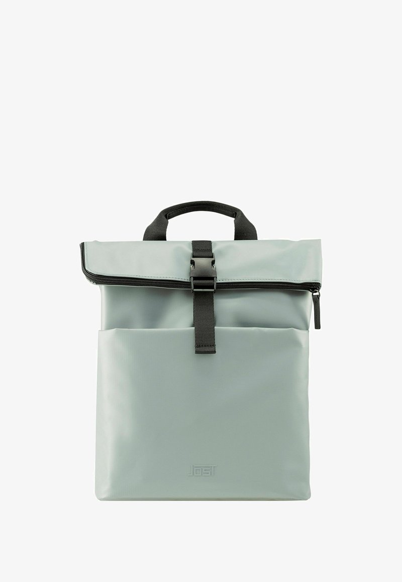 Un sac à dos gris clair avec une fermeture à enroulement, en matériau texturé, avec des accents de sangle et de matériel noirs, et un poche extérieure.