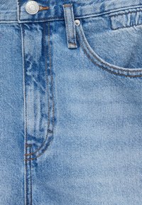 Jean en denim bleu clair en gros plan montrant la poche avant, la boucle de ceinture, le bouton métallique avec le texte « Pull & Bear Denim » et les détails de couture orange.
