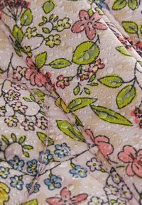Tissu à motif floral avec des dessins roses, jaunes, verts et bleus, présentant une surface texturée et de petites gouttes visibles.