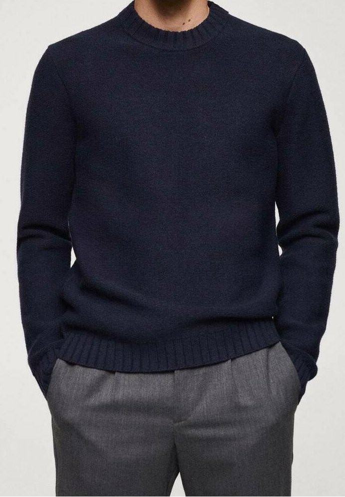 Homme portant un pull en maille bleu marine avec poignets et ourlet côtelés, assorti à un pantalon gris coupe ajustée, mains dans les poches.