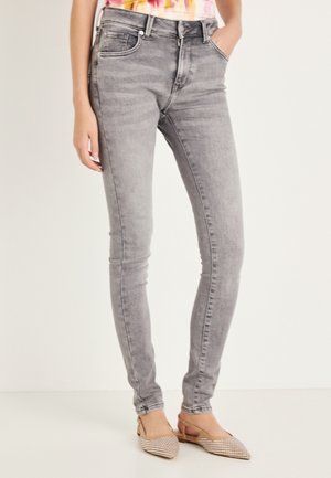 Vaqueros ajustados de cintura alta en gris con textura suave, ligero desgaste y cinco bolsillos; combinados con zapatos beige sin cordones con patrón tejido.