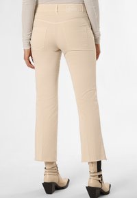 Beige Schlaghosen mit einer glatten Textur, ausgestattet mit Gesäßtaschen und einem dezenten Muster am Taillenbund, kombiniert mit cremefarbigen Knöchelschuhen.