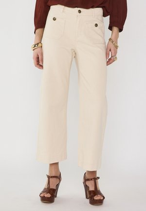 Beige wijde broek gedragen met bruine plateauhakken, gouden armbanden en ringen, gecombineerd met een bordeauxrode top met lange mouwen.