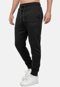 Zwarte joggingbroek met een trekkoord in de taille, taps toelopende benen en geribde manchetten. Heeft subtiele branding op het bovenbeen. Gemaakt van zachte stof.