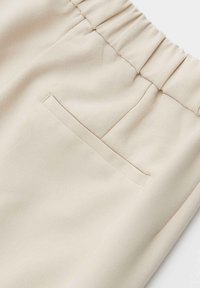 Beige broek met een elastische tailleband, voorzien van een enkele achterzak en een gladde, zachte textuur.