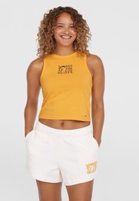 Żółty bezrękawnik crop top z czarnym napisem "KOBIETY FAL"; w połączeniu z białymi szortami z podobną pomarańczową grafiką.