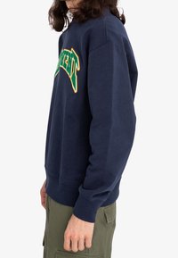 Felpa di colore blu navy realizzata in tessuto di cotone, con un logo ricamato multicolore sul petto e polsini e orlo a coste.