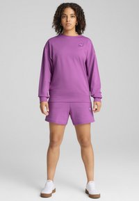 Felpa viola e pantaloni shorts coordinati realizzati in un morbido tessuto, con un piccolo logo sul petto e una vestibilità rilassata. Sneakers bianche completano il look.