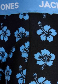 Gros plan sur un boxer noir avec un motif de fleurs d'hibiscus bleues et une ceinture bleue comportant le texte blanc partiel « JACK JONES ».