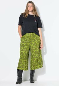 Zwarte t-shirt met een roze hartprint, gecombineerd met groene wijde broek met een bloemenpatroon en zwarte cowboylaarzen.