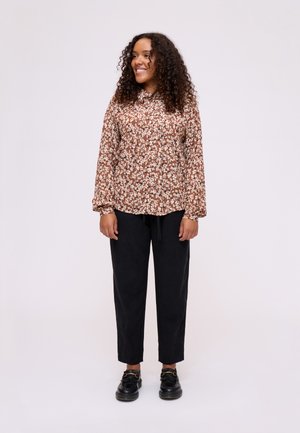 Camicia lunga a maniche con stampa floreale marrone, con scollatura arricciata, abbinata a pantaloni neri a sigaretta e scarpe nere con un accento a fibbia.