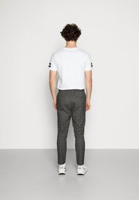Hvid t-shirt med sorte detaljer, parret med grå ternede tapered bukser. Outfittet suppleres af hvide sneakers med rød branding.