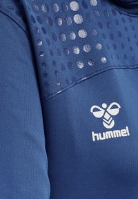 Top sportivo blu scuro con un pannello testurizzato caratterizzato da motivi circolari e un logo bianco sul petto. Tessuto morbido con un design aderente.
