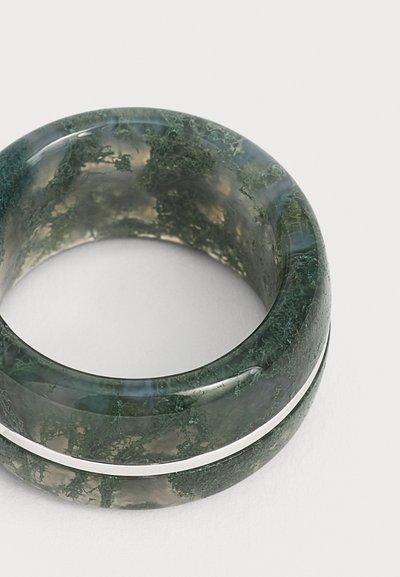 Large anneau vert translucide avec des motifs organiques ressemblant à de la mousse et une surface lisse et polie sur un fond clair.