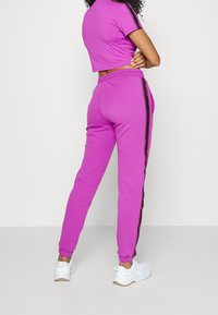 Purple cropped top paired with matching tapered sweatpants featuring black side stripes, completed with white athletic shoes.