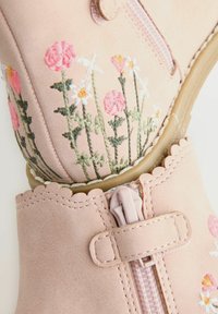 Botas de tobillo de imitación de cuero en color rosa con diseño floral bordado, borde con forma ondulada y cierre de cremallera. La superficie texturizada añade detalle.