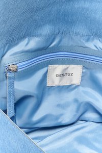 Sac à main bleu clair avec une texture semblable à de la fourrure, doté d'un intérieur en satin et d'une poche zippée bleue. L'étiquette indique "GESTUZ".