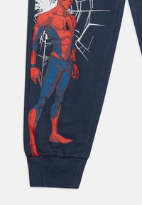 Marineblauwe pyjamabroek met een Spider-Man graphic in rood en blauw. Beschikt over ribbels aan de uiteinden en een zachte textuur. Spinnenwebdetail op de achtergrond.