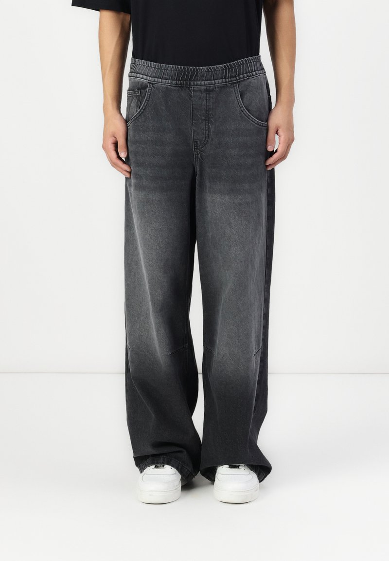 Wide-leg, dark grey denim trousers with an elastic waistband, front pockets, and faded texture. Paired with white sneakers.