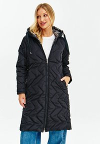 Prošívaný černý zateplený kabát s kapucí, zipovým zapínáním, bočními kapsami a květinovou podšívkou. Má délku ke kolenům a texturovanou tkaninu.