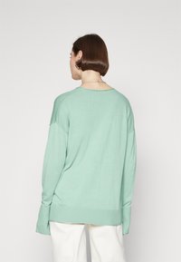 Ljusgrön, stickad tröja med avslappnad passform, neddragna axlar och ribbade ärmslut. Har en bred halsringning och en mjuk textur.