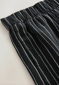 Shorts en tissu noir à rayures blanches verticales, dotés d'une ceinture élastique et d'une texture douce. Coupe décontractée.