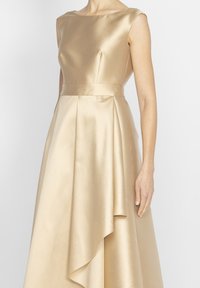 Złotą satynową sukienkę z dopasowaną górą, rękawami typu cap oraz pełną spódnicą z drapowanymi detalami i asymetrycznym dołem.