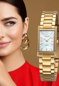 Montre en quartz rectangulaire dorée avec un cadran en nacre, accents en cristal et un bracelet en métal articulé. Des boucles d'oreilles audacieuses complètent le design.