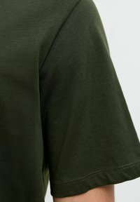 Olijfgroene katoenen t-shirt met korte mouwen, een gladde textuur en een nette stiksels langs de mouwen en de zoom.