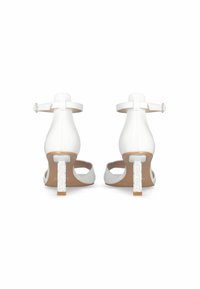 Sandales à talons en cuir blanc avec une bride de cheville, bout ouvert et un talon bloc unique avec un design décoratif. Texture lisse, style minimaliste.