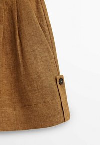 Jupe en lin marron avec un détail de bouton sur le côté et un design plissé au niveau de l'ourlet, offrant une apparence de tissu texturé et naturel.