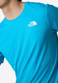 Kortärmad T-shirt med rund hals i ljus teal-tyg. Har en vit logotyp på bröstet, slät textur och atletisk passform.