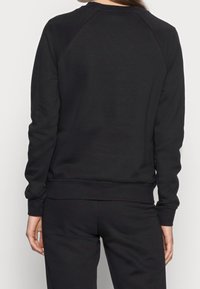 Person wearing plain black long-sleeve sweatshirt and matching black pants, shown from behind against a plain white background.