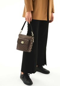 Borsa a tracolla marrone a motivo con accessori dorati, forma rettangolare e manico corto. Indossata con pantaloni neri a gamba larga e sneakers nere.