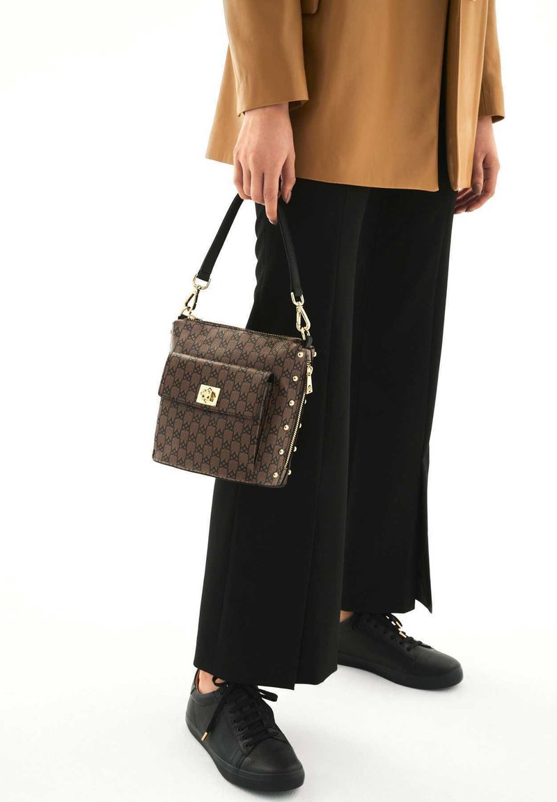 Borsa a tracolla marrone a motivo con accessori dorati, forma rettangolare e manico corto. Indossata con pantaloni neri a gamba larga e sneakers nere.
