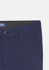 Pantalon habillé bleu marine avec fermeture à boutons, passants de ceinture et poches latérales, montrant la partie supérieure avant et l'étiquette intérieure de la ceinture.