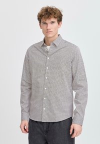 Camisa de manga larga en blanco con un patrón geométrico negro, cuello de botón y cierre frontal de un solo botón. Tejido ligero, ajuste regular.