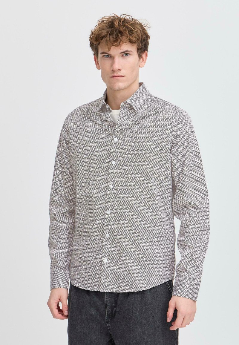 Camisa de manga larga en blanco con un patrón geométrico negro, cuello de botón y cierre frontal de un solo botón. Tejido ligero, ajuste regular.