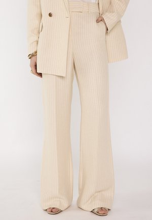 Pantaloni beige a righe larghe abbinati a giacca coordinata, braccialetti dorati, anelli e tacchi aperti beige.