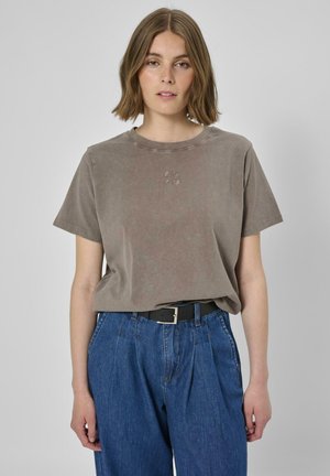 Braunes Baumwoll-T-Shirt mit rundem Ausschnitt und kurzen Ärmeln, versehen mit einer dezenten Logo-Stickerei auf der Vorderseite, kombiniert mit hochgeschnittenen blauen Jeans aus Denim.