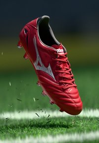 Sarkano futbola apavu izgatavoti no sintētiskā materiāla, ar elegantu dizainu, strukturētu augšdaļu un sudraba akcentiem, ar redzamām studenēm uz apakšējās daļas.