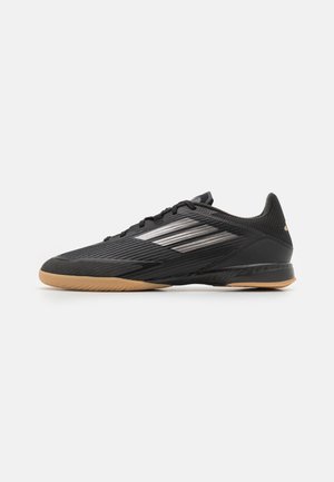Black athletic shoe with a textured mesh upper, sleek design, three silver stripes, and a gum rubber sole. Lightweight and low-profile shape.