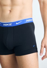 Schwarze Boxershorts mit einem blauen elastischen Bund, der das Nike-Logo trägt. Weicher Stoff, figurbetontes Design und flachnähtige Details.