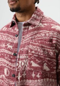 Rood-wit geruite flanellen overhemd met kraag, voorzien van een borstzak en zwarte knopen. Gestructureerde wolachtige stof met dierenmotieven.