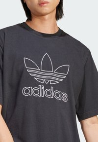Czarna bawełniana koszulka z krótkim rękawem, z białym logo adidas z trzema kształtami liści i poziomymi paskami w wzorze.