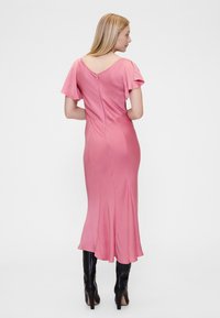 Ružičasta haljina od satena s kratkim lepršavim rukavima, V-oblaznim izrezom na leđima i uskom siluetom koja završava lepršavim rubom. Nošena s crnim čizmama do koljena.