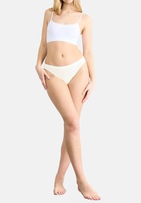 Bralette bianca con spalline sottili e slip bikini crema abbinati; entrambi presentano una texture liscia e un design minimalista.