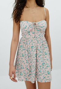 Abito a stampa floreale in rosa chiaro con fiori blu e gialli. Presenta un corpetto aderente, spalline sottili regolabili e una gonna fluida.