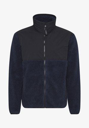 Tengerészkék bolyhos dzseki magas gallérral, kontrasztos sima anyagú felső résszel, teljes hosszúságú cipzárral és texturált testtel a melegség érdekében.